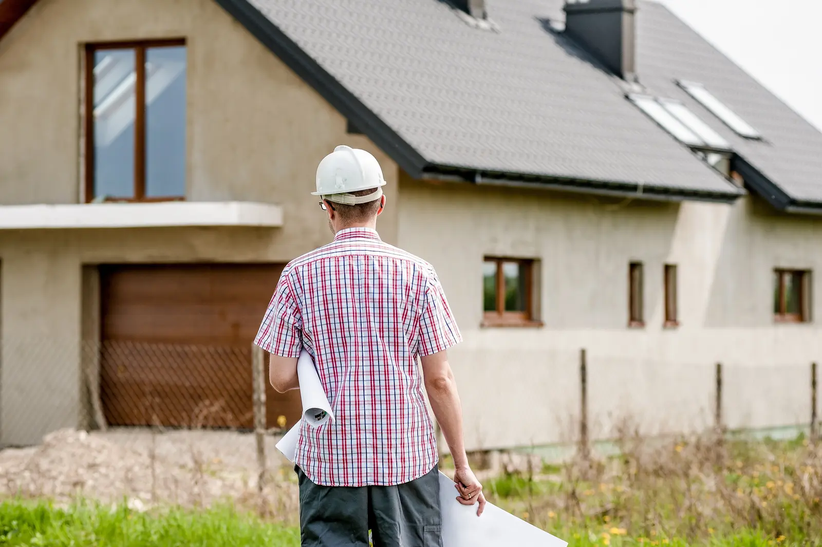 Un conducteur de travaux en casque blanc devant une maison en fin de chantier